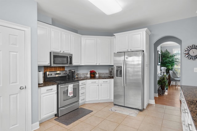 kitchen featuring dark stone countertops, white cabinets, stainless steel appliances, and light tile patterned floors