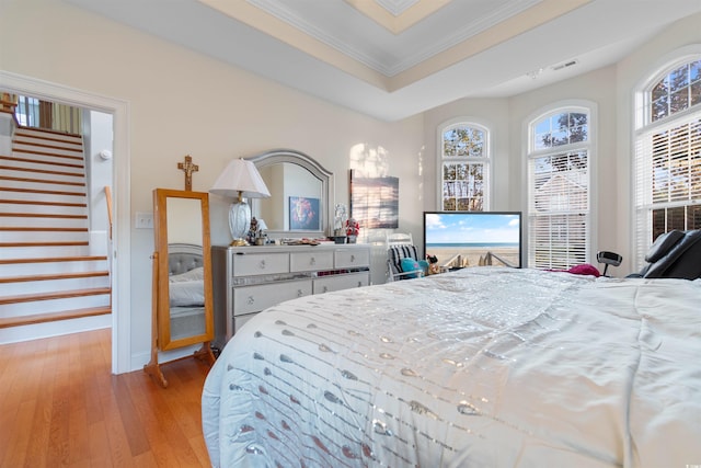 bedroom with ornamental molding, a tray ceiling, and light wood-type flooring