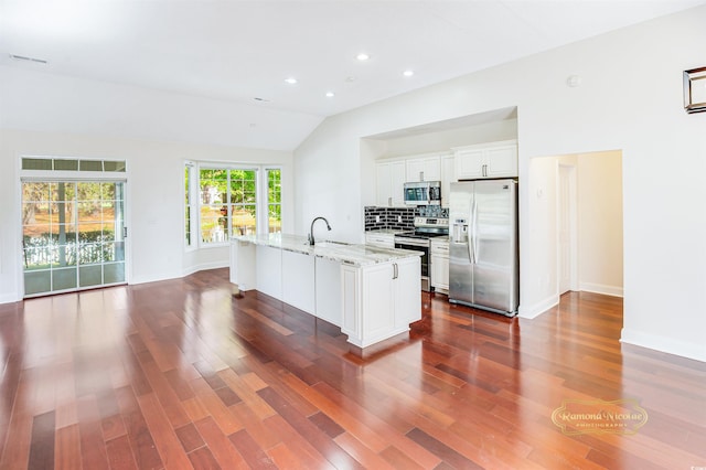 kitchen featuring stainless steel appliances, white cabinetry, dark hardwood / wood-style floors, an island with sink, and vaulted ceiling