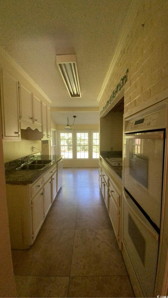 kitchen with a textured ceiling, sink, dark tile patterned floors, crown molding, and white appliances