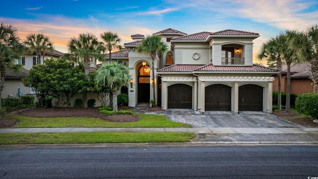 mediterranean / spanish-style home featuring a balcony, stucco siding, a garage, a tile roof, and decorative driveway