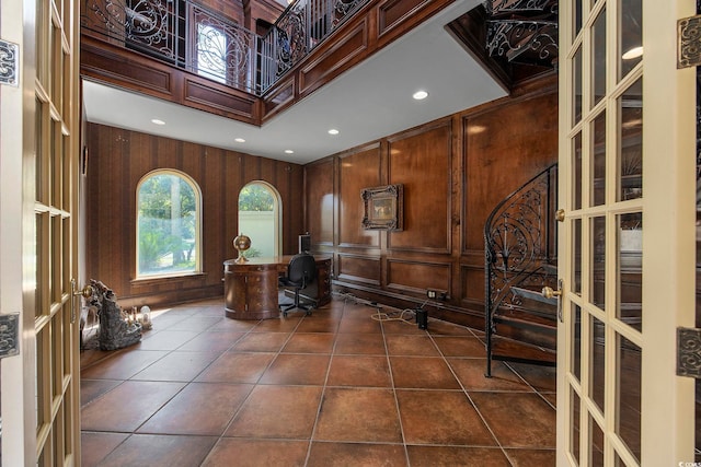 home office featuring dark tile patterned flooring, recessed lighting, wood walls, a decorative wall, and a towering ceiling