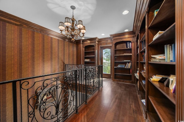 interior space with an upstairs landing, ornamental molding, dark wood-style floors, an inviting chandelier, and wallpapered walls