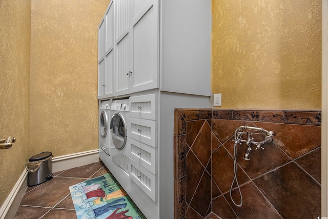 laundry area with baseboards, washing machine and clothes dryer, cabinet space, tile patterned floors, and a textured wall