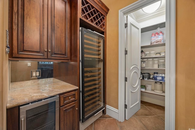 kitchen with crown molding, wine cooler, light stone counters, and light tile patterned flooring