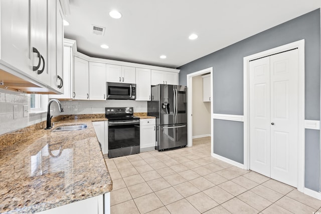 kitchen featuring appliances with stainless steel finishes, light tile patterned flooring, sink, white cabinets, and light stone counters