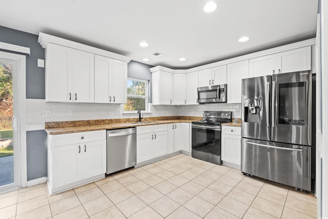 kitchen featuring appliances with stainless steel finishes, white cabinets, dark stone countertops, and sink