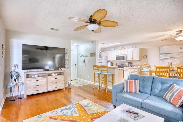 living room with light wood-type flooring, a textured ceiling, and ceiling fan