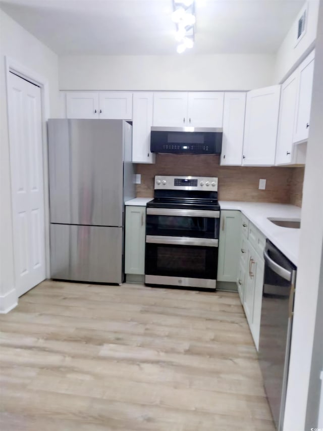 kitchen featuring appliances with stainless steel finishes, light wood-type flooring, decorative backsplash, and white cabinetry