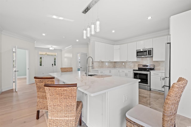 kitchen with appliances with stainless steel finishes, a kitchen island with sink, white cabinets, and a breakfast bar