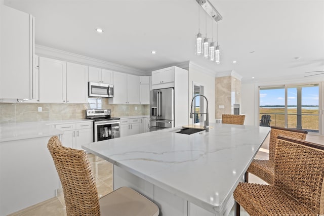 kitchen with sink, an island with sink, white cabinets, appliances with stainless steel finishes, and a kitchen bar