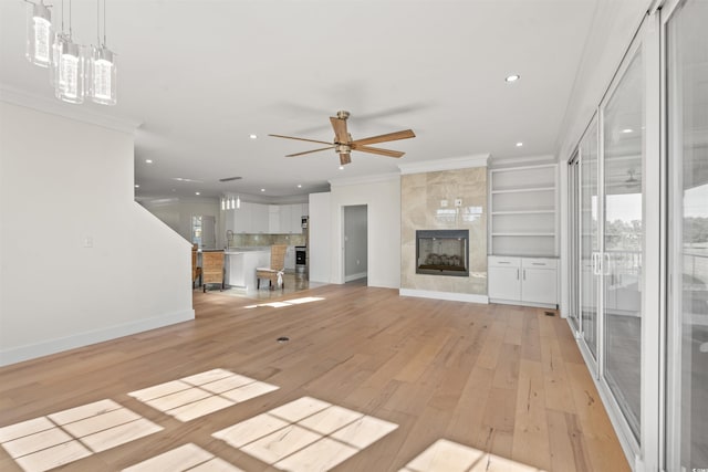 unfurnished living room featuring a fireplace, built in features, crown molding, and light wood-type flooring