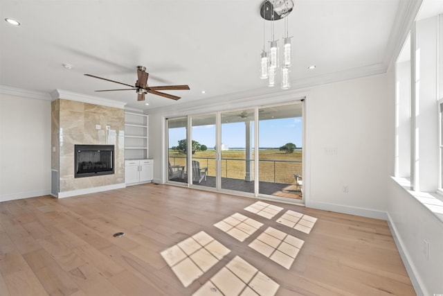 unfurnished living room with ceiling fan with notable chandelier, a fireplace, built in features, light hardwood / wood-style flooring, and ornamental molding