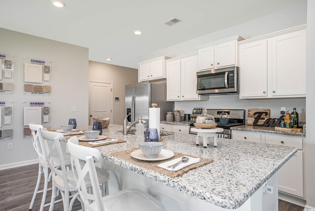 kitchen featuring dark wood-type flooring, stainless steel appliances, white cabinetry, and a kitchen island with sink