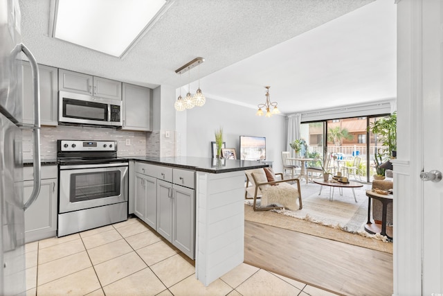 kitchen with kitchen peninsula, gray cabinetry, stainless steel appliances, pendant lighting, and light tile patterned floors