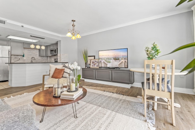 living room featuring sink, crown molding, a notable chandelier, and light hardwood / wood-style flooring