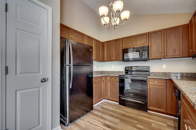 kitchen featuring black appliances, hanging light fixtures, vaulted ceiling, a notable chandelier, and light hardwood / wood-style floors