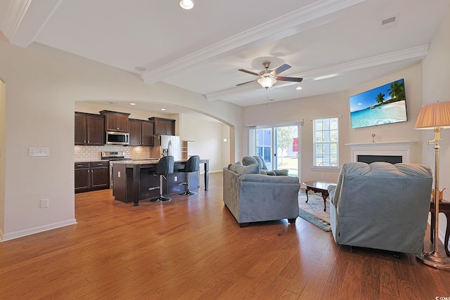 living room with ceiling fan, ornamental molding, light hardwood / wood-style flooring, and beam ceiling