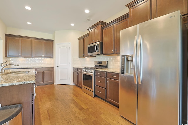 kitchen featuring light wood-type flooring, sink, tasteful backsplash, stainless steel appliances, and light stone countertops