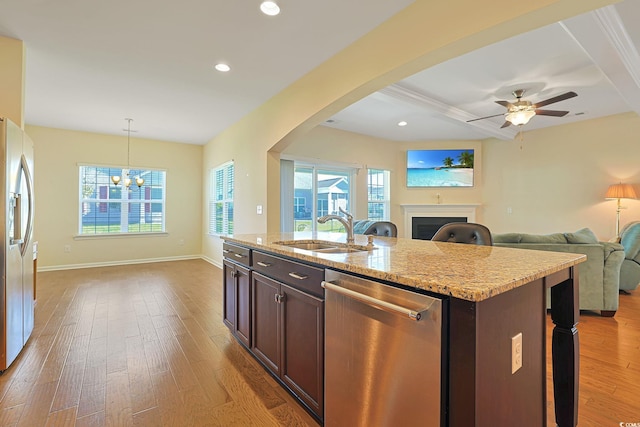 kitchen with wood-type flooring, stainless steel appliances, sink, hanging light fixtures, and a center island with sink