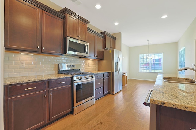 kitchen with light wood-type flooring, light stone countertops, stainless steel appliances, sink, and hanging light fixtures