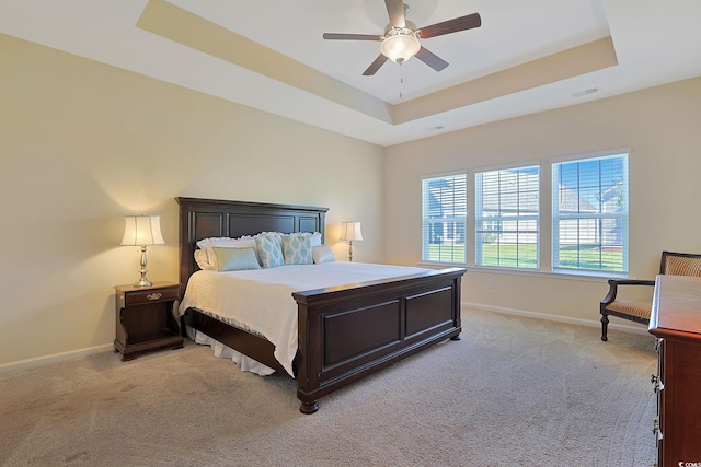 bedroom featuring ceiling fan, light colored carpet, and a tray ceiling