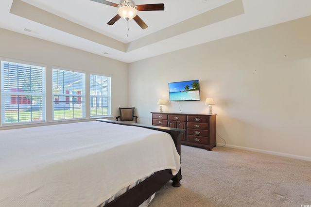 bedroom with ceiling fan, a tray ceiling, and light colored carpet