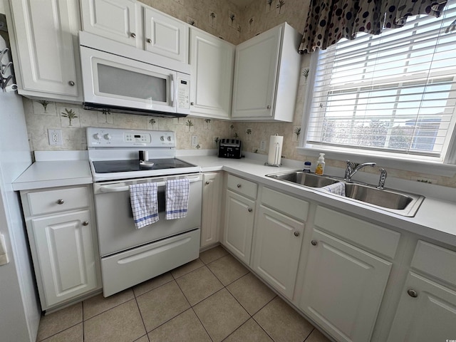 kitchen with white cabinetry, sink, light tile patterned floors, and white appliances