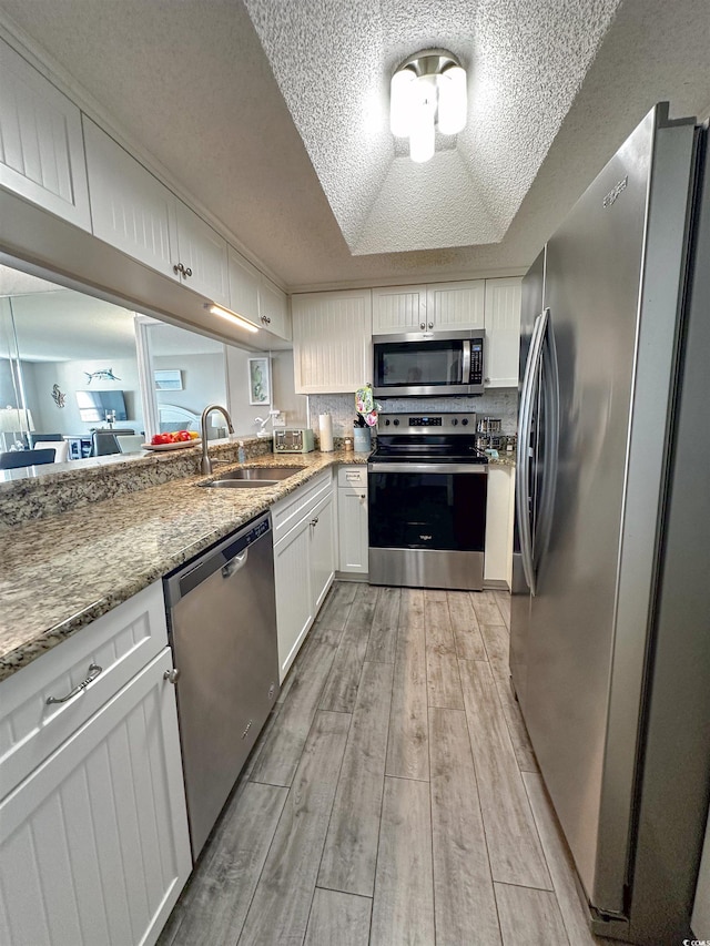 kitchen featuring sink, a tray ceiling, white cabinetry, light hardwood / wood-style floors, and stainless steel appliances