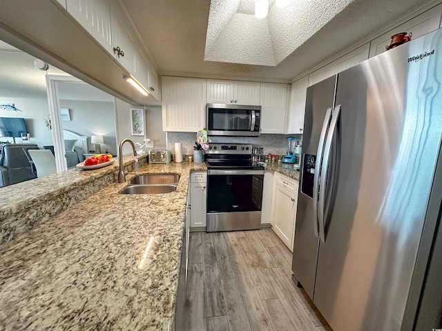 kitchen featuring appliances with stainless steel finishes, white cabinetry, light stone countertops, light hardwood / wood-style floors, and sink