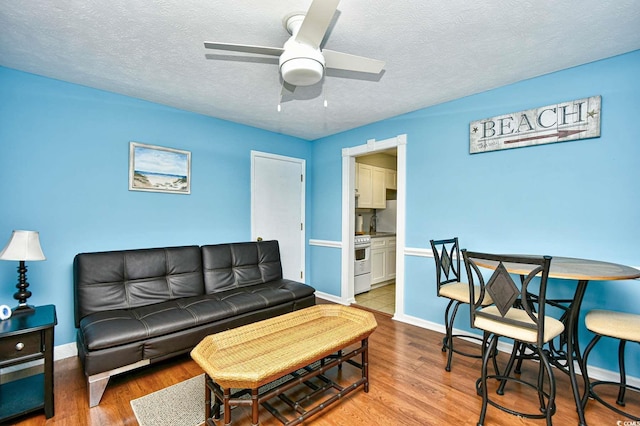 living room with wood finished floors, a ceiling fan, baseboards, and a textured ceiling