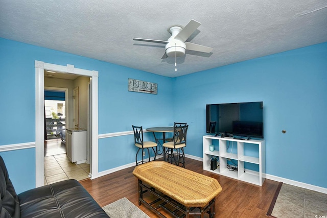 living area featuring baseboards, a ceiling fan, wood finished floors, and a textured ceiling