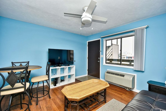 living room featuring wood-type flooring, ceiling fan, a wall unit AC, and a textured ceiling