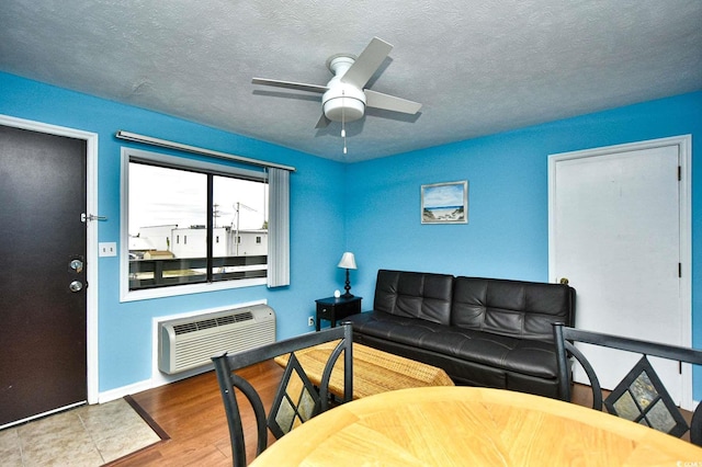 living area featuring an AC wall unit, a ceiling fan, wood finished floors, and a textured ceiling
