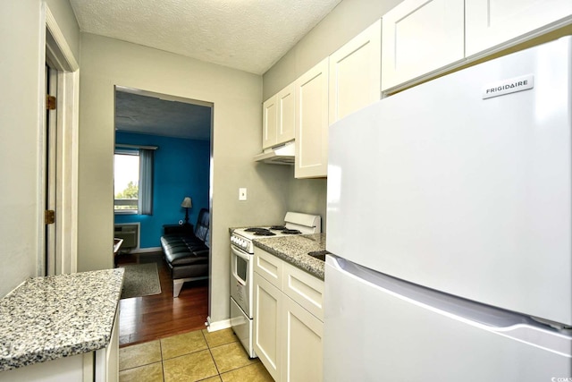 kitchen featuring light wood-type flooring, gas range, light stone counters, white cabinets, and white fridge