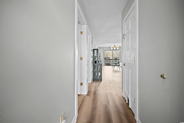 hall with a notable chandelier, a textured ceiling, and wood-type flooring