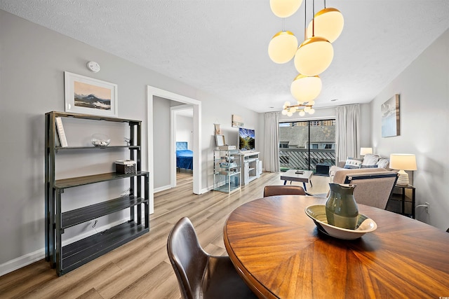 dining area featuring light hardwood / wood-style flooring, a textured ceiling, and an inviting chandelier