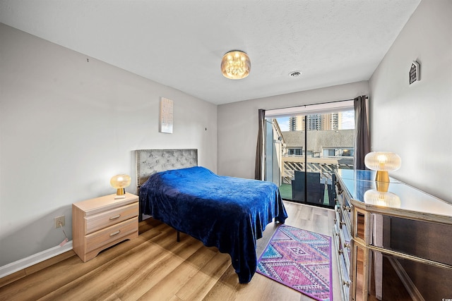 bedroom with access to outside, a textured ceiling, and hardwood / wood-style floors