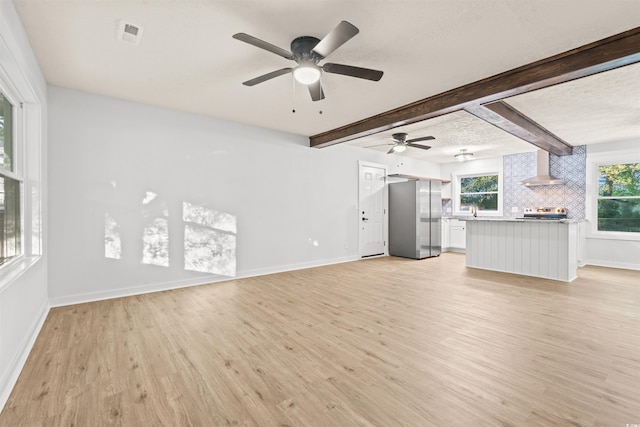 unfurnished living room with ceiling fan, beamed ceiling, light hardwood / wood-style flooring, and a textured ceiling