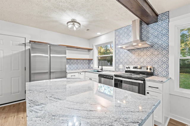 kitchen with stainless steel appliances, wall chimney range hood, white cabinets, and light wood-type flooring