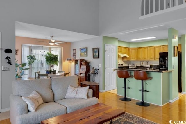 living room with a high ceiling, light wood-type flooring, and ceiling fan