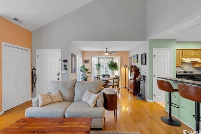 living room with light hardwood / wood-style flooring, high vaulted ceiling, and ceiling fan