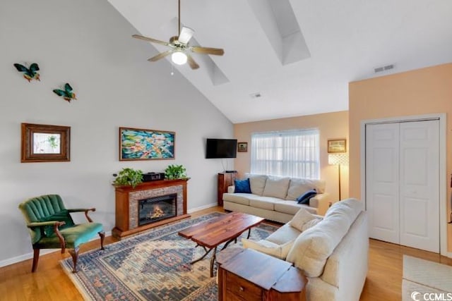 living room with light hardwood / wood-style floors, high vaulted ceiling, a fireplace, and ceiling fan