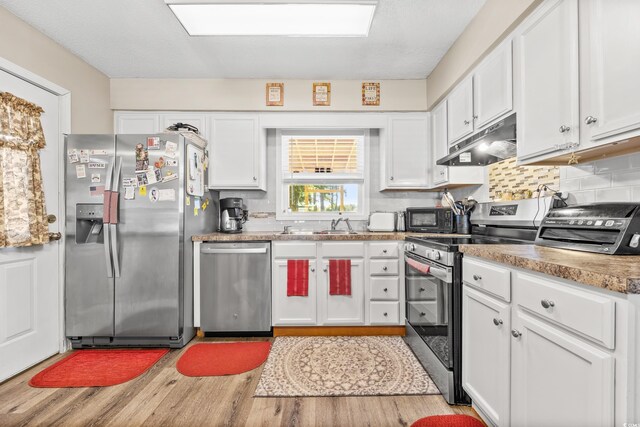 kitchen featuring a textured ceiling, appliances with stainless steel finishes, white cabinetry, decorative backsplash, and light hardwood / wood-style floors