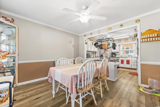 dining room featuring a textured ceiling, sink, ornamental molding, ceiling fan, and light hardwood / wood-style flooring