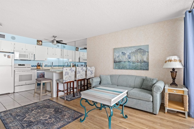 living room with light hardwood / wood-style flooring, a textured ceiling, and ceiling fan