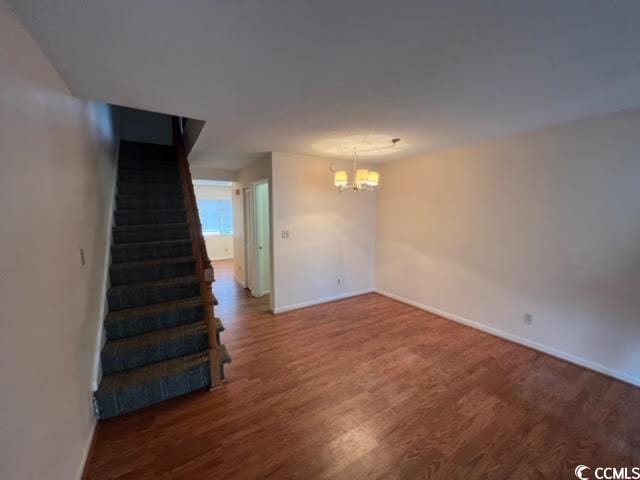 spare room featuring an inviting chandelier and dark wood-type flooring