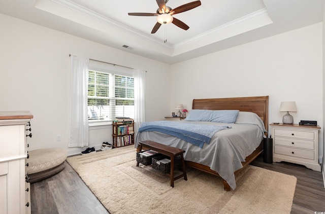 bedroom featuring ornamental molding, dark wood-type flooring, ceiling fan, and a raised ceiling