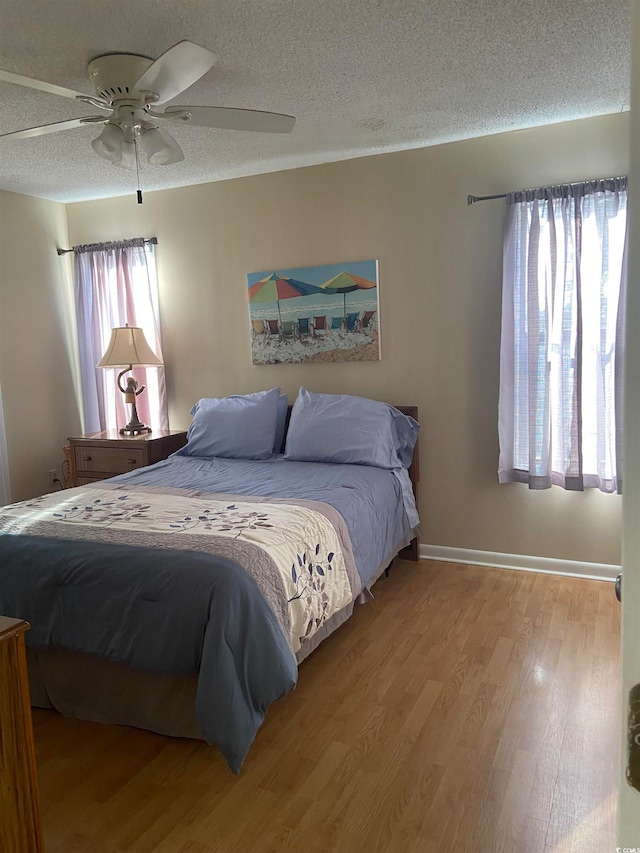 bedroom with ceiling fan, hardwood / wood-style flooring, a textured ceiling, and multiple windows