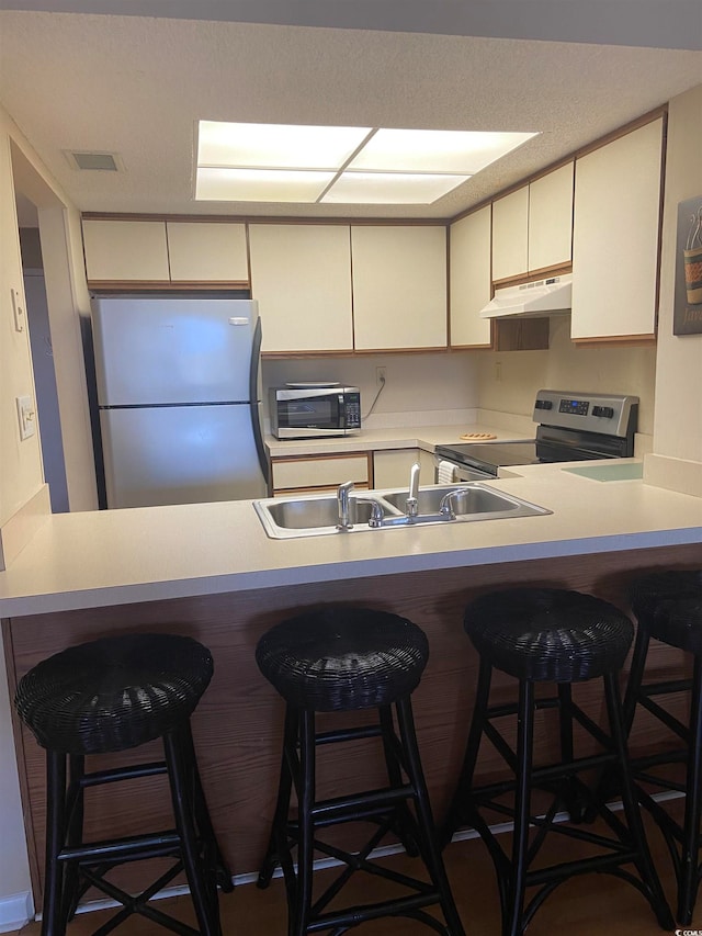 kitchen featuring appliances with stainless steel finishes, a breakfast bar, a textured ceiling, and sink